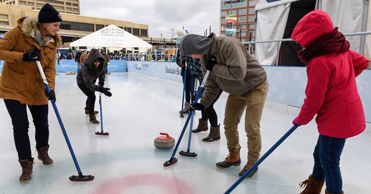 A family learning the sport of curling on an ice rink